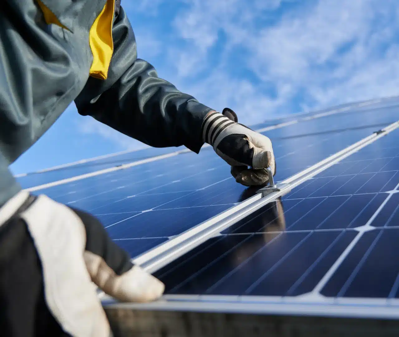 Technician adjusting solar panel under blue sky.